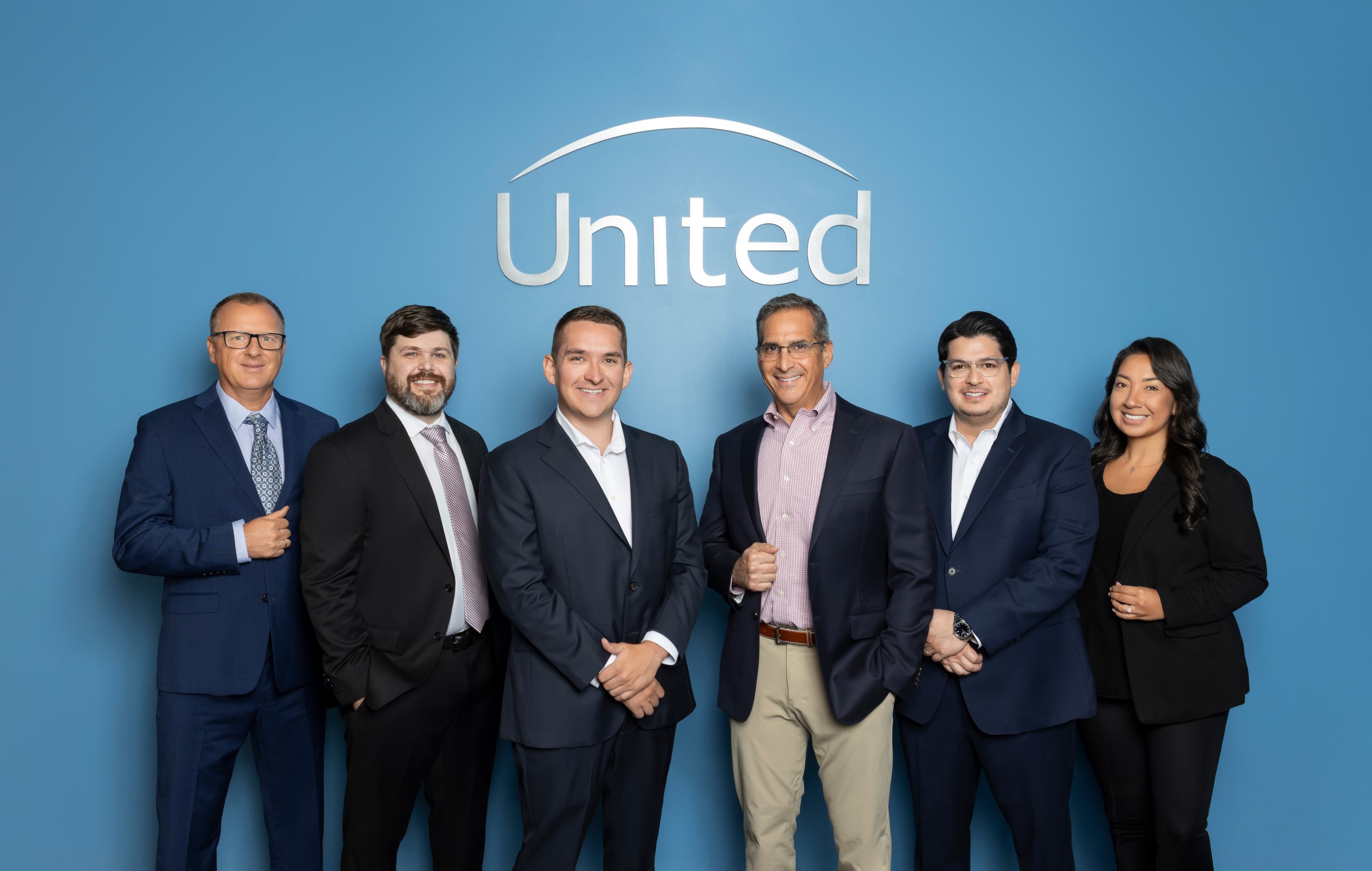The United Financial Planning Group team — six advisors standing together in front of a blue wall with the United logo